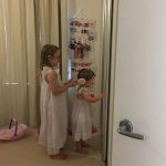 A little girl standing brushing another girls hair in front of a mirror